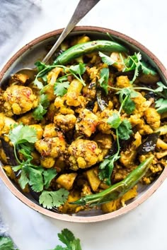 a bowl filled with cauliflower, green beans and cilantro on top of a white table