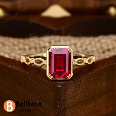 a red stone ring sitting on top of a wooden box with gold trimmings