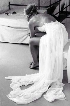 a woman sitting on top of a bed next to a white sheet covered mattress in a room