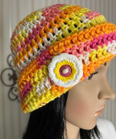 This is a crochet hat with a flipped brim. The brim is attached to the hat with a flower shaped button. The hats color is called Warm Brights. It includes orange, yellow, fuschia and white.  The button is 1 3/4 inches. It has textured white and yellow "petals" and a fuschia center.  One size fits most. 100% Acrylic yarn. Acrylic button. For best results hand wash, lay flat to dry. Yellow Knitted Crochet Hat For Spring, Spring Multicolor Cloche Hat With Curved Brim, Yellow Knitted Beach Hat, Yellow Adjustable Crochet Hat For Spring, Adjustable Yellow Crochet Hat For Spring, Yellow Crochet Hat For The Beach, Yellow Crochet Cap Hat, Spring Adjustable Yellow Crochet Hat, Hand Knitted Adjustable Mini Hats For Spring