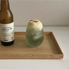 a bottle of beer and a glass on a wooden tray with foamy drink in it