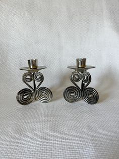 two metal candlesticks sitting on top of a white cloth