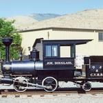 a black train engine sitting on the tracks in front of a white building and trees