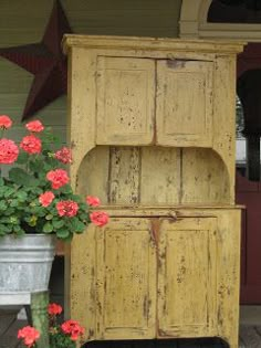 an old wooden cabinet with flowers in the pot on the front porch, next to it is a flower planter