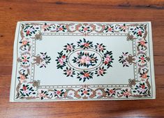 a white place mat with pink and green flowers on it sitting on a wooden floor