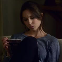 a young woman sitting on a couch reading a book in the dark with her legs crossed