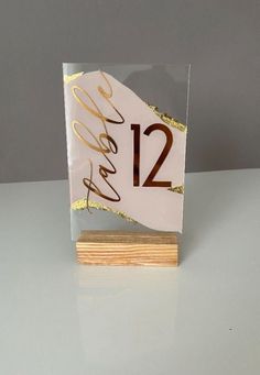 a small white and gold table number on a wooden stand with a name tag attached to it