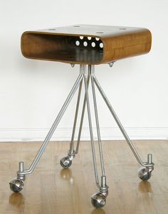 a wooden table with four metal legs and three holes on the top, sitting on a hard wood floor in front of a white wall