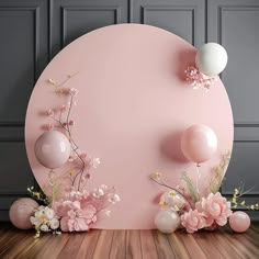 a pink wall with balloons and flowers on the floor in front of an oval backdrop