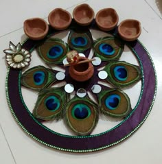 peacock feathers are arranged in a circle on the floor with small bowls and a candle holder