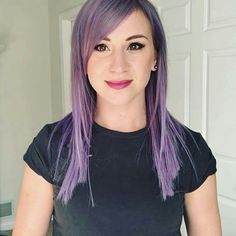 a woman with purple hair and black shirt posing for the camera in front of a white door