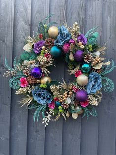 a wreath with blue and purple flowers hanging on a wooden wall next to a fence