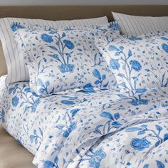 a bed with blue and white flowers on the comforter, pillows and pillow cases