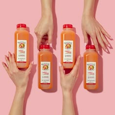 three bottles of orange juice being held by two hands against a pink background with the same bottle in each hand