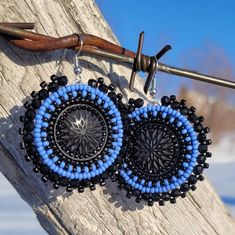 two blue and black beaded earrings hanging from a hook on a piece of wood