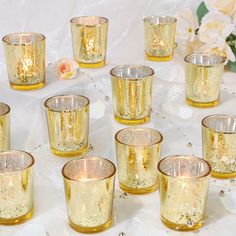 a table topped with lots of gold colored glasses filled with liquid next to white flowers