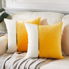 three yellow and white pillows sitting on top of a couch next to a plant in a vase