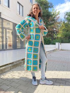 a woman standing in front of a building wearing a crocheted coat and sneakers