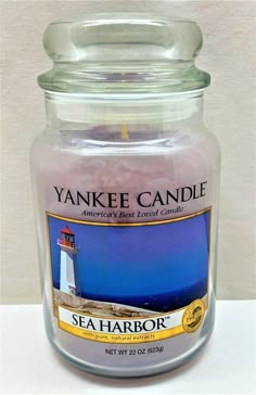 yankee candle jar with sea harbor lighthouse in the front and blue sky behind it on a white surface