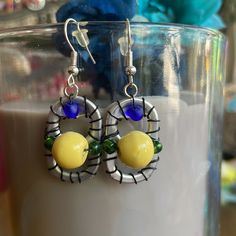 a pair of yellow and blue earrings sitting on top of a glass cup next to a vase