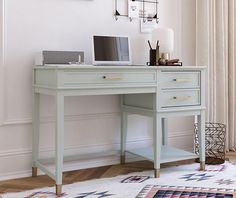 a desk with a laptop on it in front of a white wall and rugs