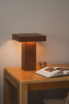 an open book sitting on top of a wooden table next to a light that is turned on