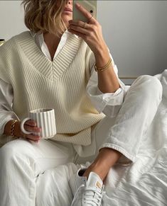 a woman sitting on top of a bed holding a cup