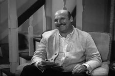 a man sitting on top of a couch in front of a stair case holding a book