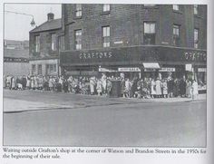 an old black and white photo of people standing in front of a store on a street corner