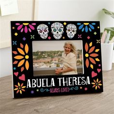 a photo frame with two sugar skulls and flowers on the front, sitting on a table next to a potted plant