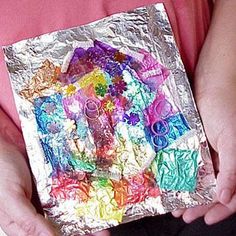 a person holding a piece of tin foil with various colored candies on it