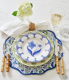 a blue and white plate with flowers on it next to silverware, wine glasses and napkins