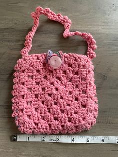 a pink crocheted purse sitting on top of a wooden table next to a ruler