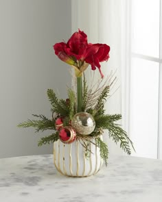 a vase filled with red flowers and greenery on top of a white table next to a window