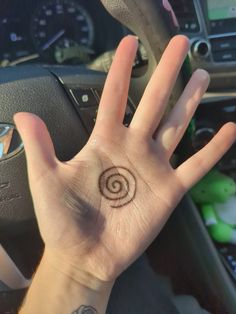 a person's hand with a small tattoo on the middle of their palm, in front of a steering wheel