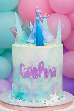 a frozen princess cake with the name carolina on it and balloons in the back ground