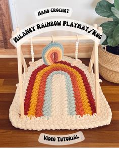 a crocheted rainbow play mat on the floor next to a potted plant