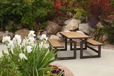 two wooden benches sitting next to each other in front of flowers and rocks on the ground