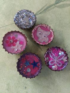 four pink and purple bottle caps with an owl on the top one is decorated with sequins