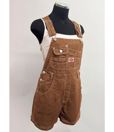 Short overalls with a multi pocket bib and logo patch detail. Traditional straps with clasp closures. Pockets on the front and back with button closures at the sides. Looks great paired with crop tops. SMALL: Waist: 26" | Hips: 40" | Inseam: 3.5" MEDIUM: Waist: 28" | Hip: 42" | Inseam: 3.5" LARGE: Waist: 30" | Hip: 44" | Inseam: 3.75" Material | 100% Cotton (Non-Stretchy Canvas/Denim) Care Instructions | Machine Wash or Hand Wash Cold  Measurements | 30" or 76 cm Top to Bottom 3.5" or 9 cm Inseam [Measured on a size Small] Model is 5'8 and wearing a size Small SMALL CUSTOMER REVIEWS 1. I'm 5'4 about 120 pounds and I ordered a small in the navy. They fit perfectly! I would recommend getting the size you usually wear. The fabric and stitching feel high quality. 2. The overalls are just great Brown Overalls Shorts, Overalls Tank Top Outfit, Utility Style Overalls With Bib Front And Suspenders, Utility Style Overalls With Suspenders And Bib Front, Utility Overalls With Suspenders And Bib Front, Utility Bib Front Overalls With Suspenders, Utility Shortalls With Adjustable Bib Front, Utility Overalls With Button Closure, Utility Shortalls With Adjustable Straps And Bib Front