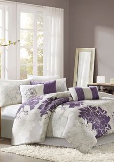 a bed with purple and white comforters in a room next to a mirror on the wall