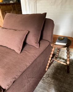 a brown couch sitting on top of a wooden floor next to a table with a book