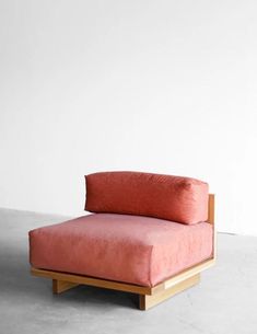 a pink couch sitting on top of a cement floor next to a white wall and wooden frame