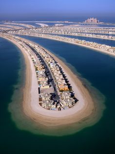 an island in the middle of water surrounded by sand and palm trees, with buildings on both sides