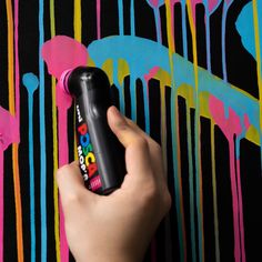 a hand holding a spray bottle in front of a colorful wall