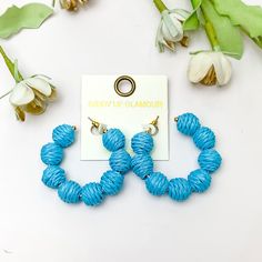 Sorbet Summer Raffia Ball Hoop Earrings in Blue. Pictured on a white background with flowers above the earrings. Summer Beach Dangle Hoop Earrings, Beach Dangle Hoop Earrings, Summer Beach Multicolor Hoop Earrings, Vibrant Beach Earrings, Vibrant Blue Summer Earrings, Giddy Up Glamour, Beach Hat, Sale Items, Hoop Earrings