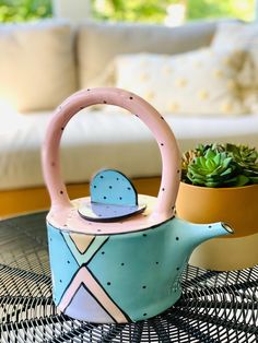 a blue teapot with a pink handle sitting on top of a table next to a potted plant