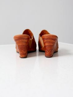 "This is a pair of 1950s vintage tooled leather wedges. The southwestern heels feature a tooled floral pattern. They have an inside elastic band for width. The slender open to sandals have a wedge heel. Brand: Campos CONDITION In good condition with wear consistent with age and use. Light usage wear to sole, insoles, and elastic band. Lovely patina to leather. MARKED SIZE: 8 FITS LIKE: 7.5 MEASUREMENTS Insole Length: 10\" .. 25.4 cm Width: 3.25\" .. 8.3 cm Height: 3\" .. 7.6 cm 91804" Spring Vintage High Heel Clogs, Vintage Brown Mules For Summer, Vintage Brown Mules With Leather Sole, Vintage Summer Clogs With Round Toe, Vintage Brown Leather Mules, Vintage Closed Toe Summer Clogs, Vintage Closed Toe Clogs For Summer, Retro Leather Slip-on Mules, Western Style Round Toe Heels For Summer