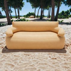 an inflatable couch sitting on the sand near some trees and beachfronts