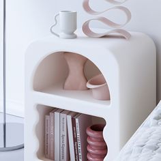 a white shelf with books and vases on it next to a bed in a room